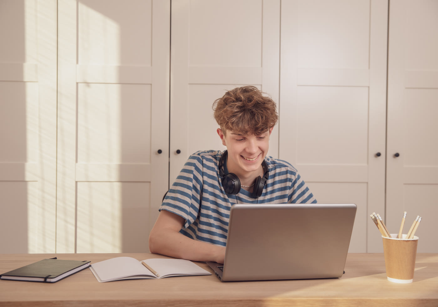Teen learner working independently with headphones and a laptop at home